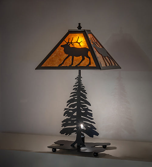 Lone elk table lamp with amber mica shade glowing and pine tree base silhouette