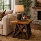 Oil Derrick Copper Side Table styled in a cozy rustic-modern living room beside a cream sofa, featuring a distressed copper-finish top, geometric wood base, warm table lamp, and stone fireplace accents.