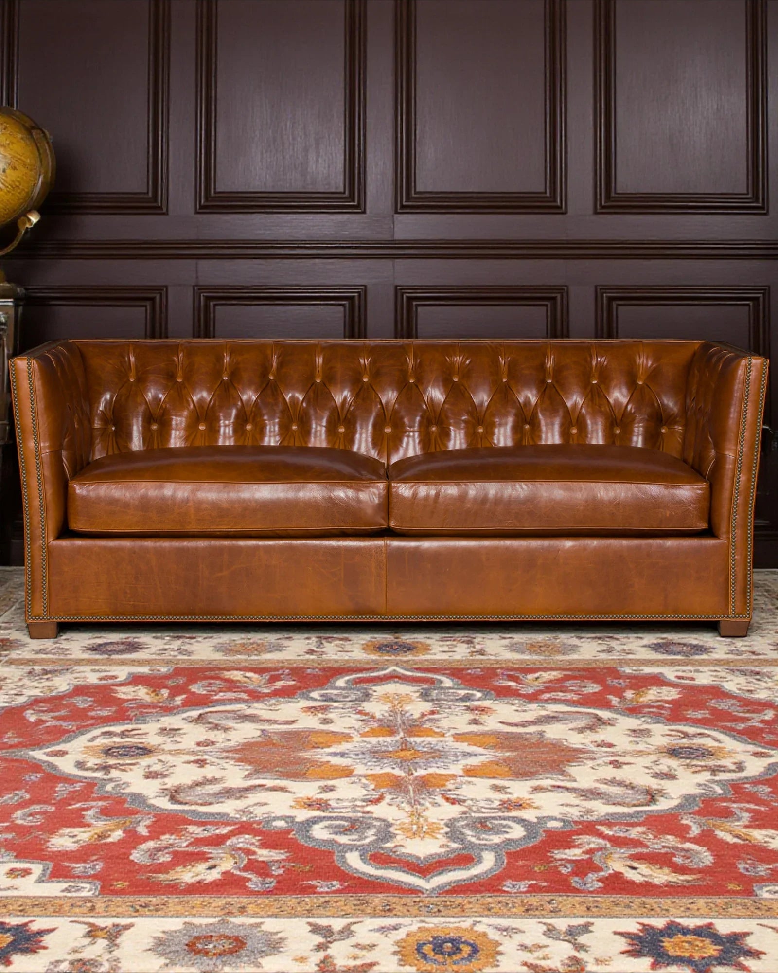 Brown leather sofa in a room with dark paneling and a patterned rug - Your Western Decor