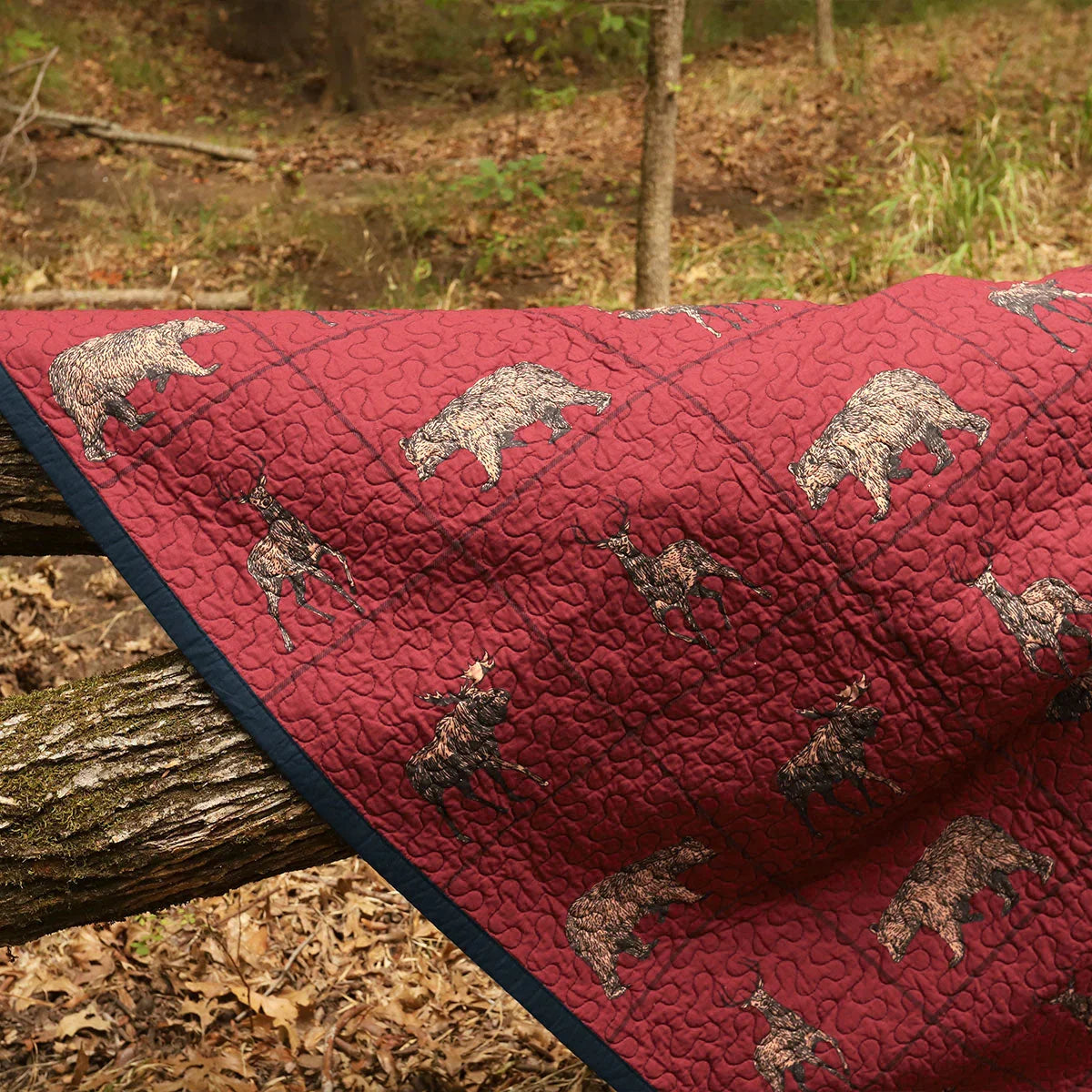 Red quilt with bear pattern draped over a log in a forest setting