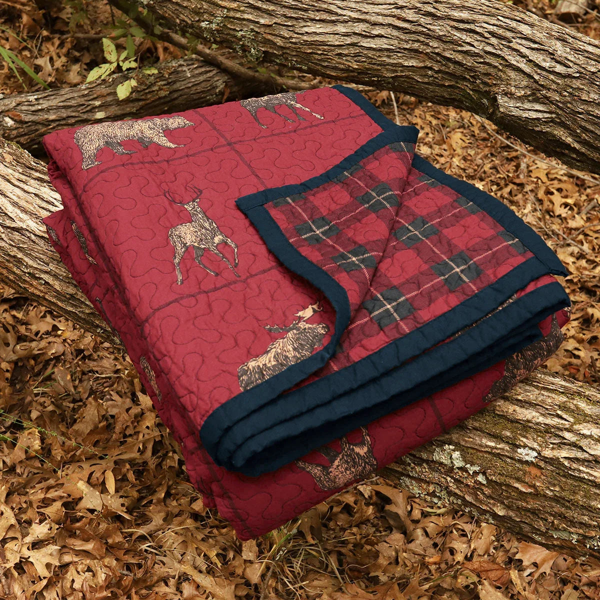 Red quilt with deer pattern on a log surrounded by leaves