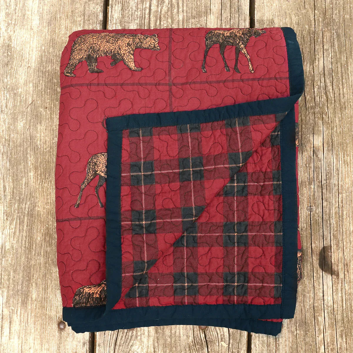 Red quilt with black border and animal patterns on a wooden surface