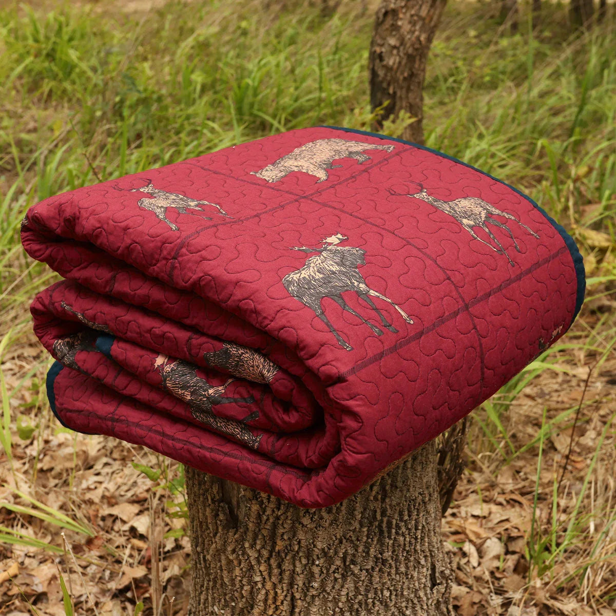 Folded red quilt with deer patterns on a tree stump in a natural setting