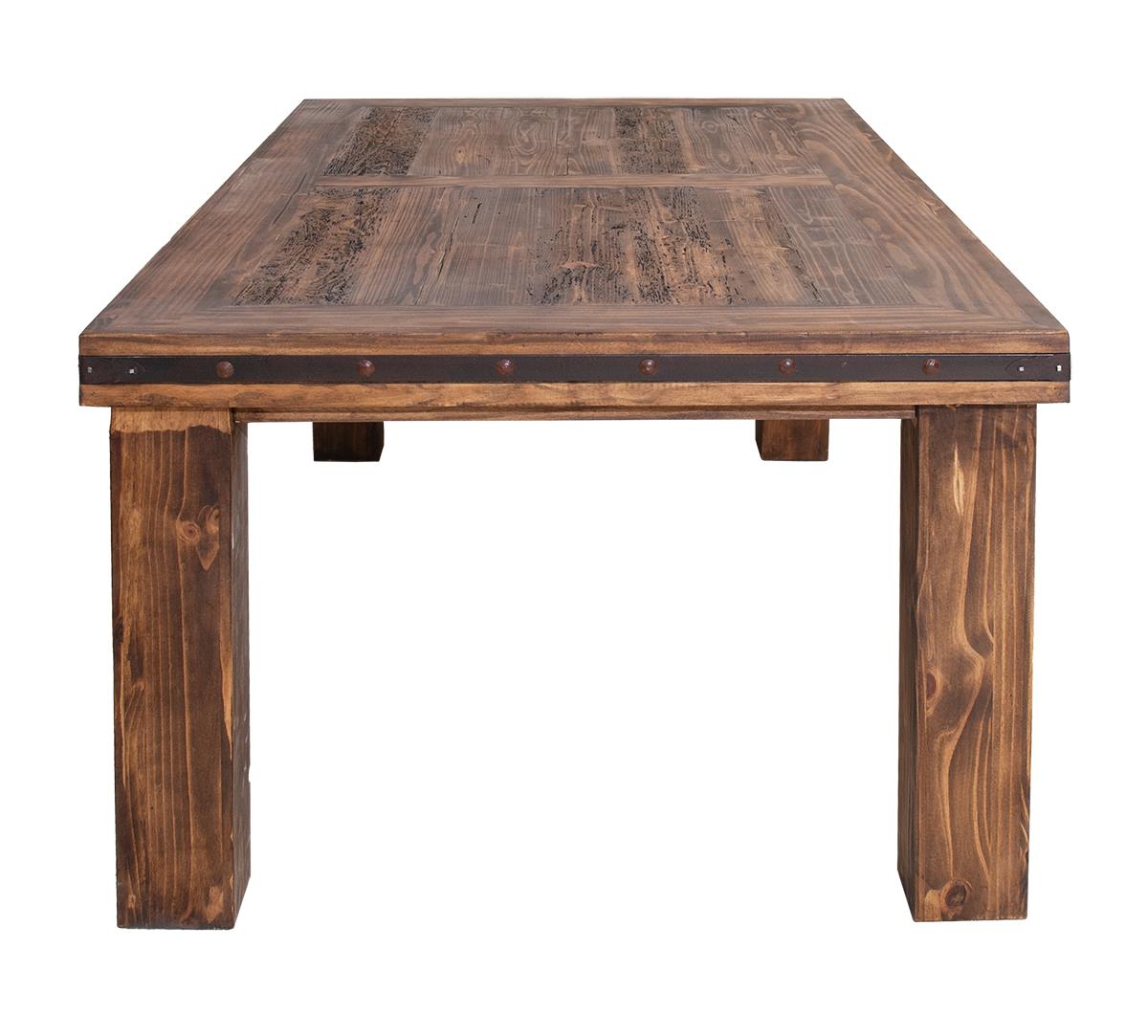 A rustic rectangular wooden dining table with a dark brown plank top, thick block legs, and dark metal trim with brass rivets along the front edge, shown against a plain white background.