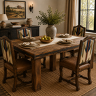 A rustic rectangular wooden dining table with four upholstered chairs in a warm, styled dining room. The table has dark brown wood with black metal hardware, and the chairs feature brown leather seats and backs with cream, blue, and red geometric patterned upholstery.
