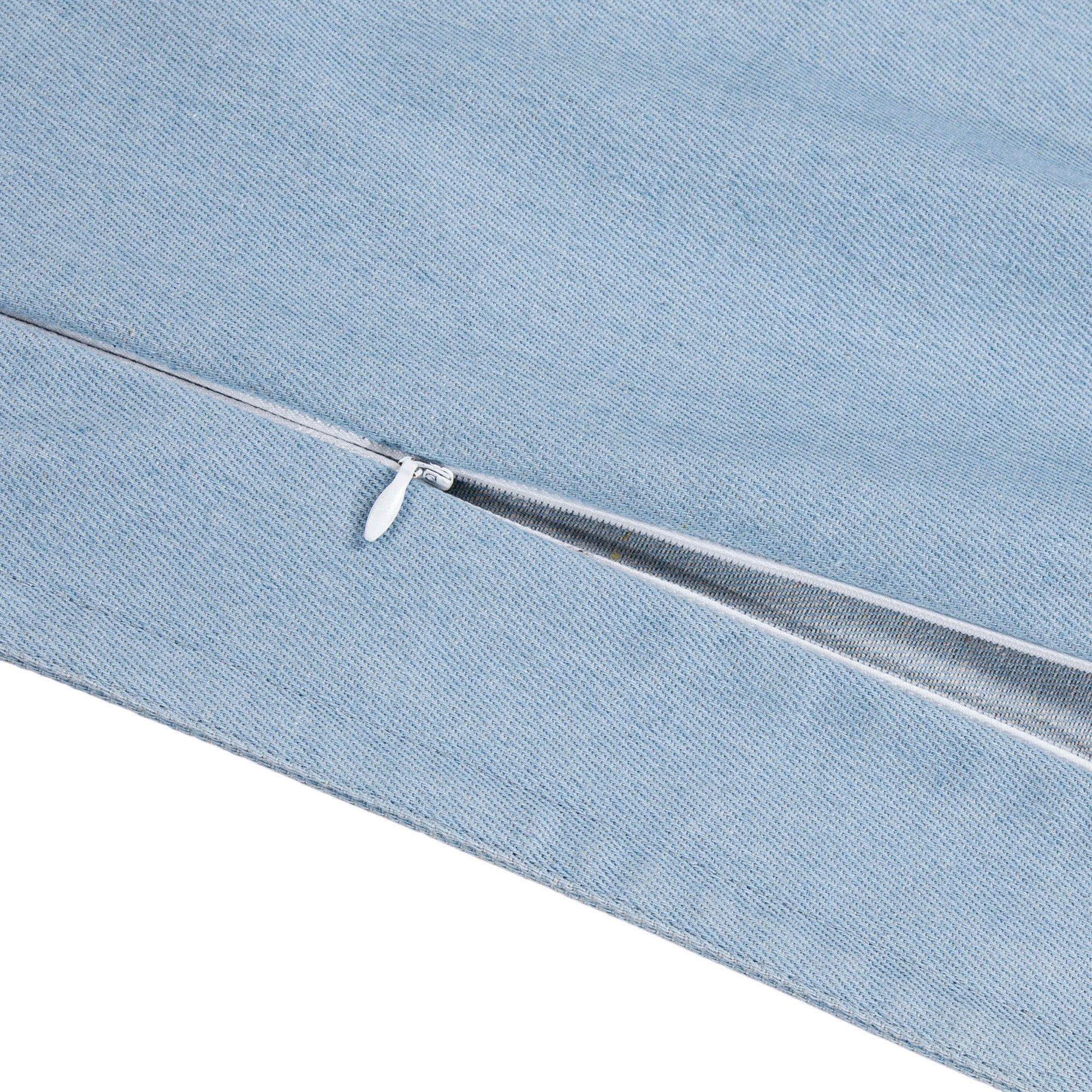 A close-up of a light blue denim pillow cover, showing a white metal zipper along the edge against a white background.