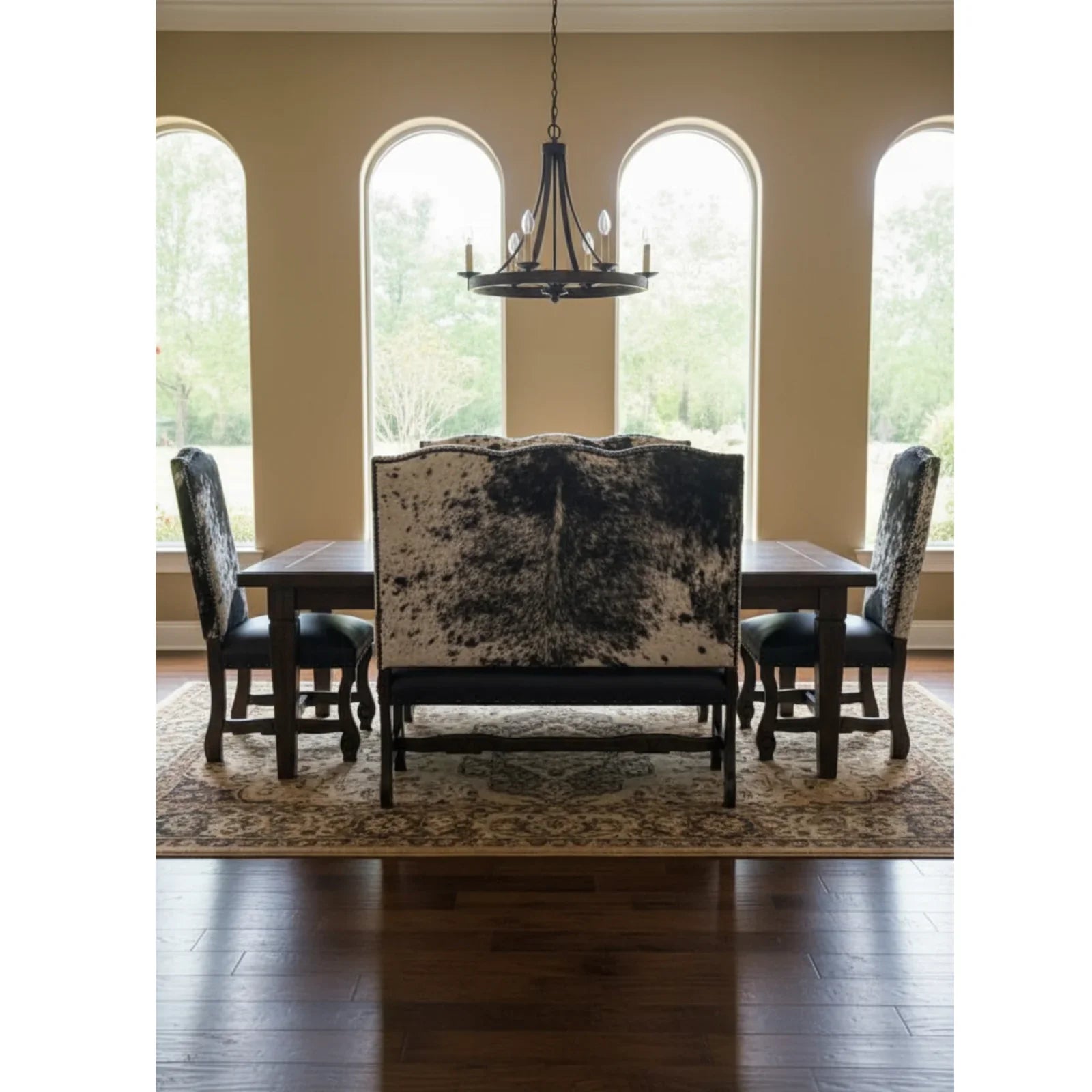 Dining room with a cowhide bench and upholstered chairs in front of large windows.