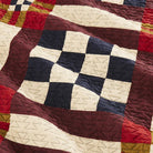 Close-up of a patchwork quilt with geometric patterns in red, blue, and beige.