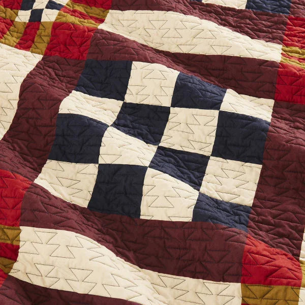 Close-up of a patchwork quilt with geometric patterns in red, blue, and beige.