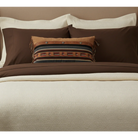 Brown and beige bedding set with decorative pillows on a bed.