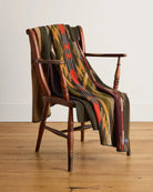 Colorful patterned blanket draped over a wooden chair on a wooden floor.