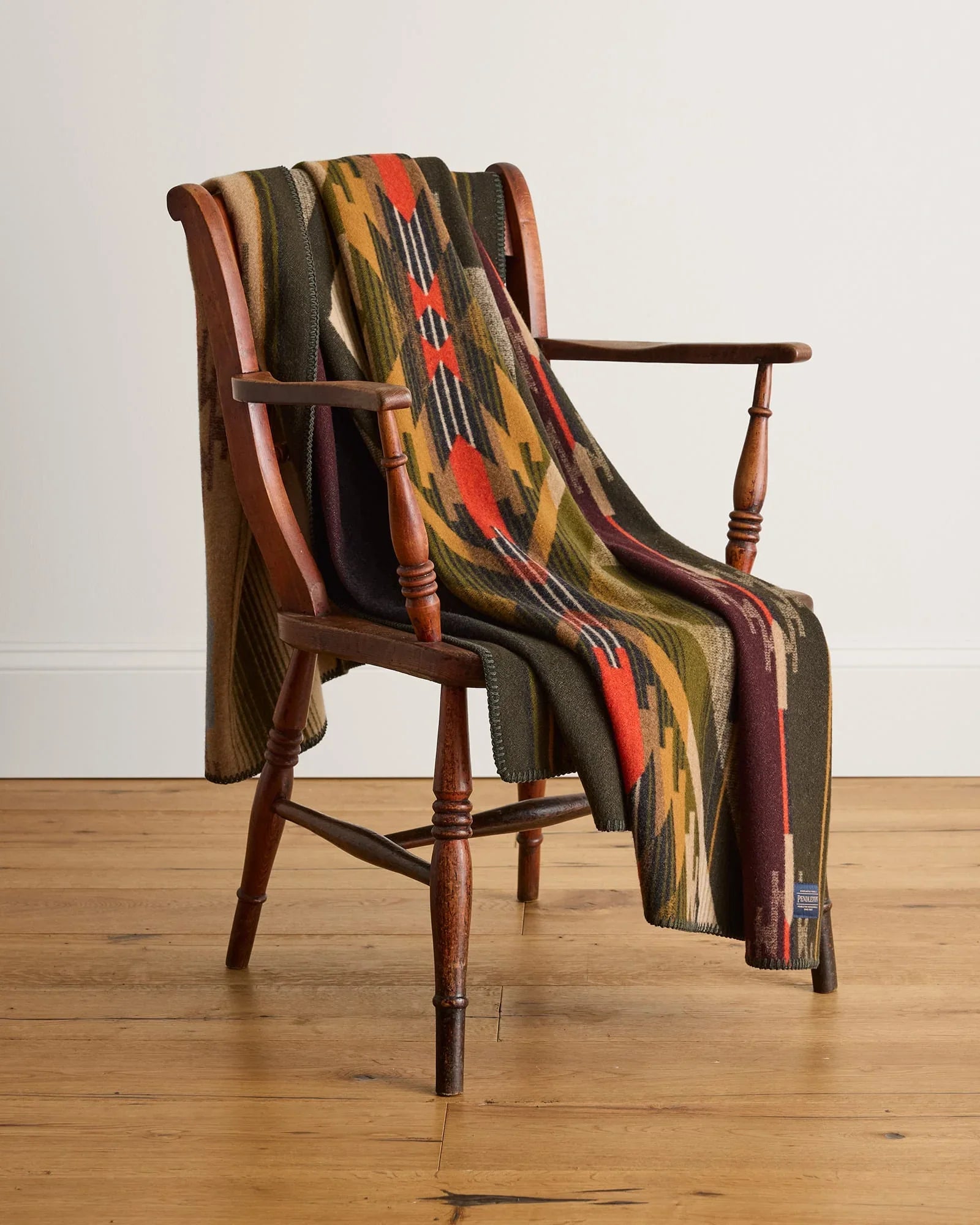 Colorful patterned blanket draped over a wooden chair on a wooden floor.
