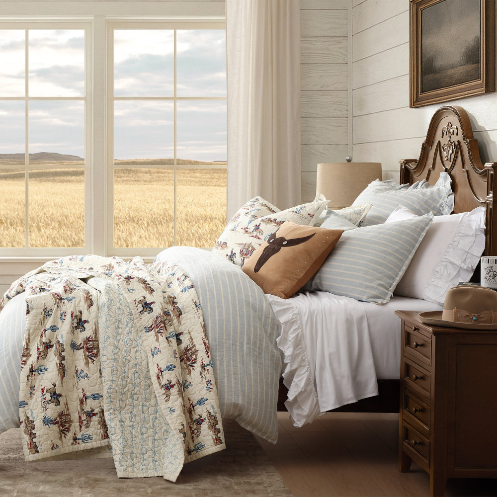 Bedroom with a large window showing a western range cowboy print quilt with striped duvet and white ruffled sheets
