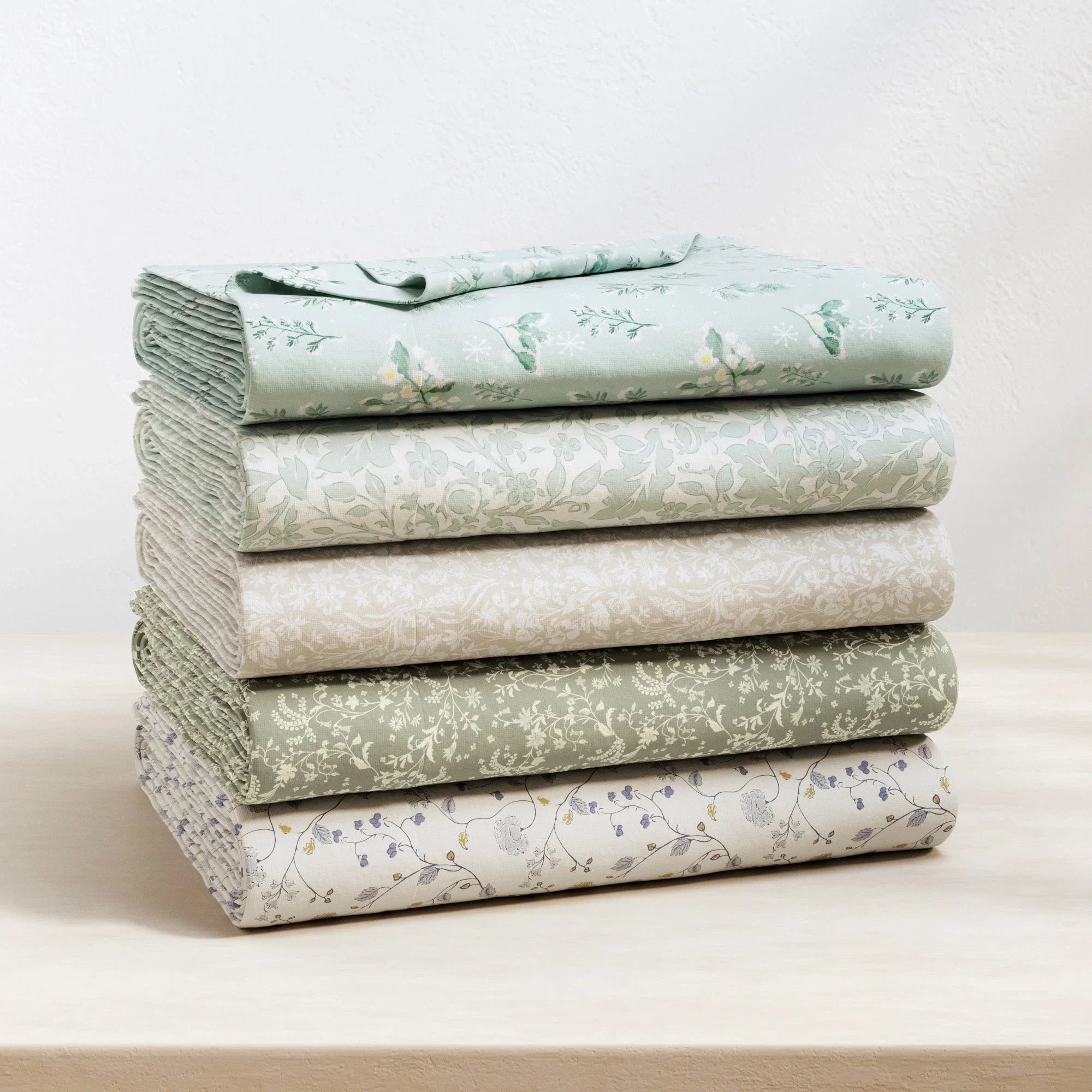 Stack of folded fabric sheets with floral patterns on a light background