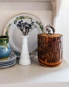 Decorative items including a white vase with dried flowers, a wooden container with a squirrel figurine, and ceramic plates on a white surface.