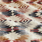 Close-up of a quilt with geometric pattern in red, blue, and brown on a white background