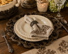 Acanthus Estate charger plate styled beneath cream stoneware dinnerware on a rustic dining table.