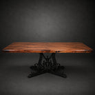 A rustic rectangular wooden dining table with a rich brown live-edge top and a black wrought-iron scrollwork pedestal base, set against a dark gray studio background.
