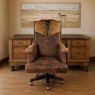 Axis hide and distressed brown leather Western office chair with nailhead trim and hardwood swivel base with executive desk with leather surface and canvas framed Antelope art