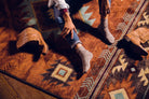 Lady sitting on Aztec Whiskey River Southwestern area rug in rust with turquoise and brown geometric diamond patterns