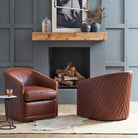 Two brown leather swivel armchairs in a styled living room setting with a fireplace, gray paneled wall, and a small side table.
