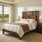 Custom upholstered barnwood bed handcrafted from reclaimed red oak with leather and patterned fabric headboard panels, styled in a bright rustic ranch bedroom with large window and neutral bedding.