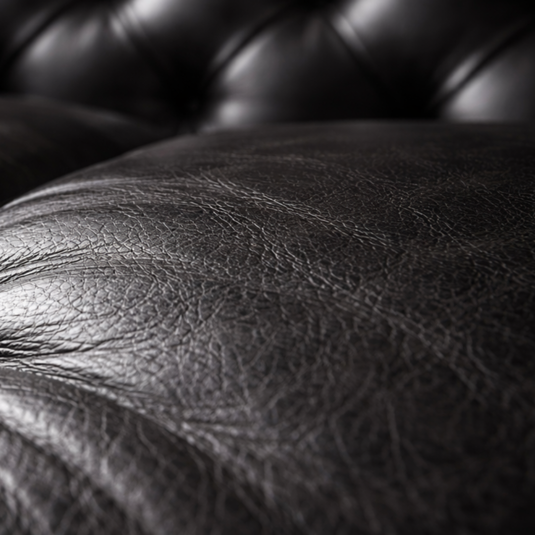 Close-up of a black leather surface with visible grain texture and tufted upholstery in the background.