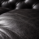 Close-up of a black leather surface with visible grain texture and tufted upholstery in the background.