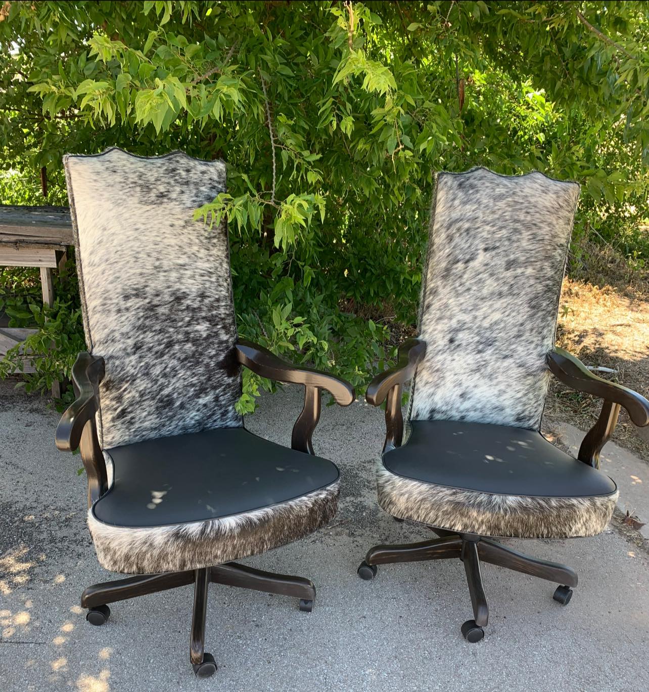 Two western office chairs with peppered cowhide-patterned backrests and black leather seats outdoors.
