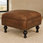 Blacksmith Ridge brown leather ottoman with turned legs and nailhead trim 