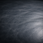 Close-up of dark blue gray textured leather with visible grain and subtle sheen.