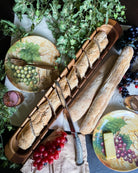 Bread display with decorative plates featuring grapes and a fork, surrounded by greenery and fruits - Your Western Decor
