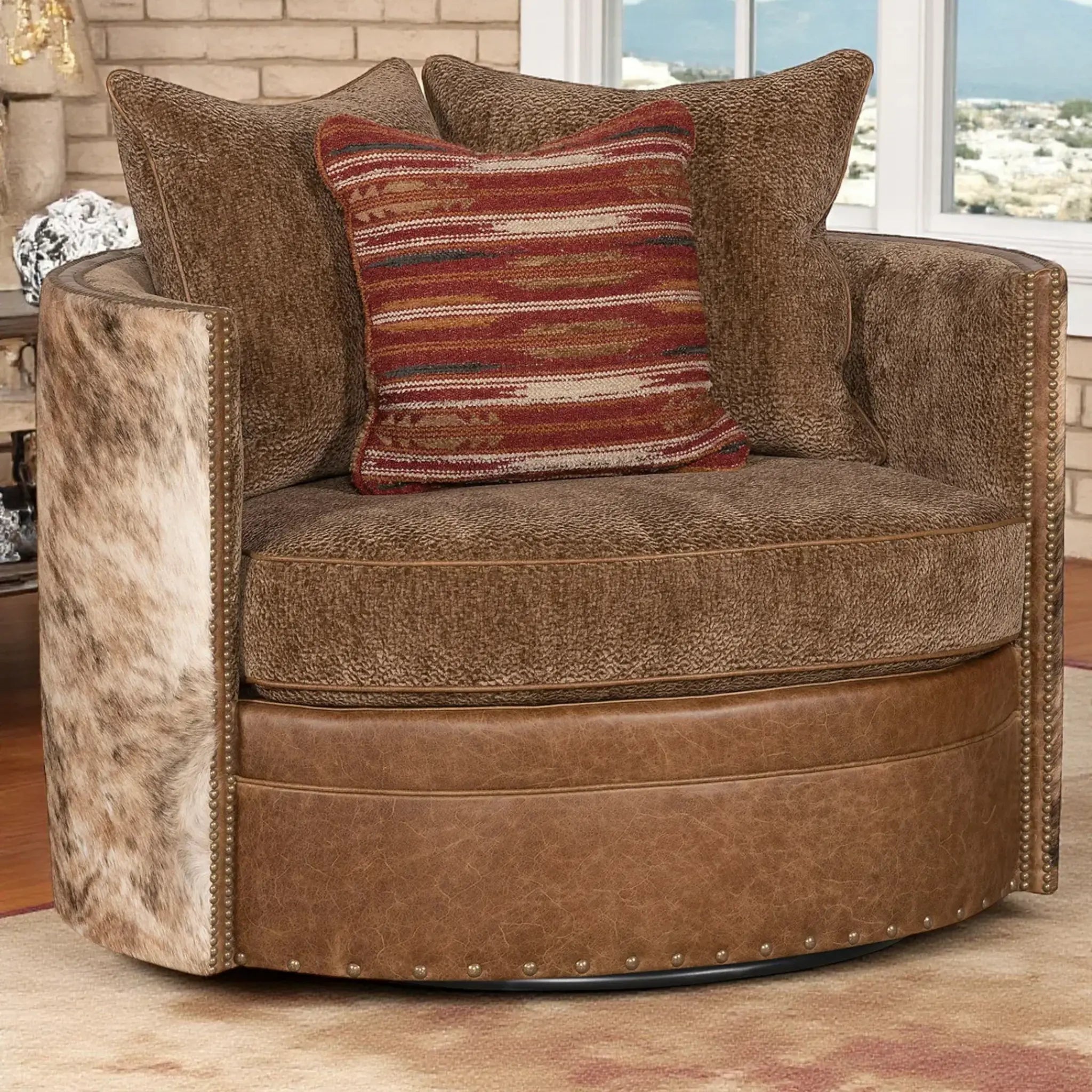 A round swivel armchair in brown textured fabric with brindle cowhide side panels and nailhead trim, styled with brown pillows and a red striped accent pillow in a living room setting.