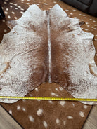 Brown peppered cowhide rug on a floor with a measuring tape for scale