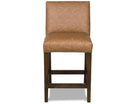A single upholstered bar stool with a warm tan faux-leather seat and backrest, dark brown wooden legs, and nailhead trim along the front edge, shown against a plain white background.