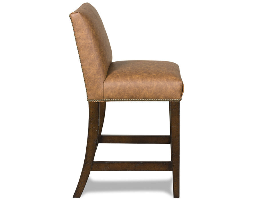 A single counter stool with a tan leather upholstered seat and backrest, dark brown wooden legs, and nailhead trim, shown against a plain white background.