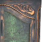 Close-up of an ornate carved wooden cabinet door with a textured green reptile-pattern glass insert and a rope detail across the top.