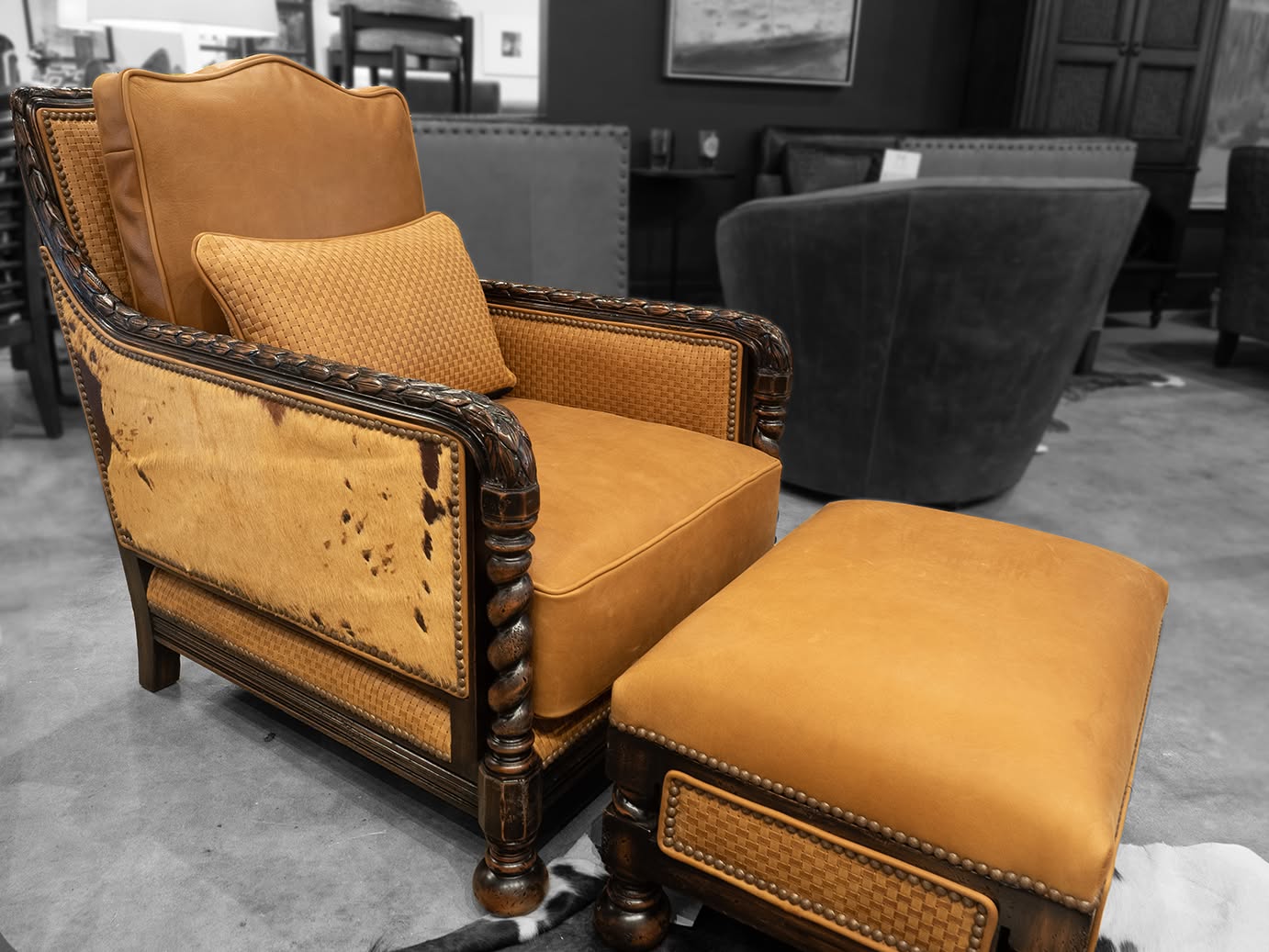 A vintage-style upholstered armchair with a matching ottoman in a warm mustard-yellow fabric, set against a blurred black-and-white showroom background.