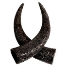 Two dark carved steer horn accessories with intricate embossed scrollwork, crossed over each other on a plain white background.