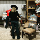 Person wearing a black hat and black jacket standing in a workshop with chairs and patterned cushions 