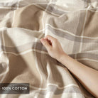 Hand touching a plaid fabric with '100% Cotton' label - Your Western Decor