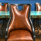 A high-back brown leather dining chair with a textured crocodile-embossed finish, black wood frame, and silver nailhead trim, positioned in front of a turquoise and black table.