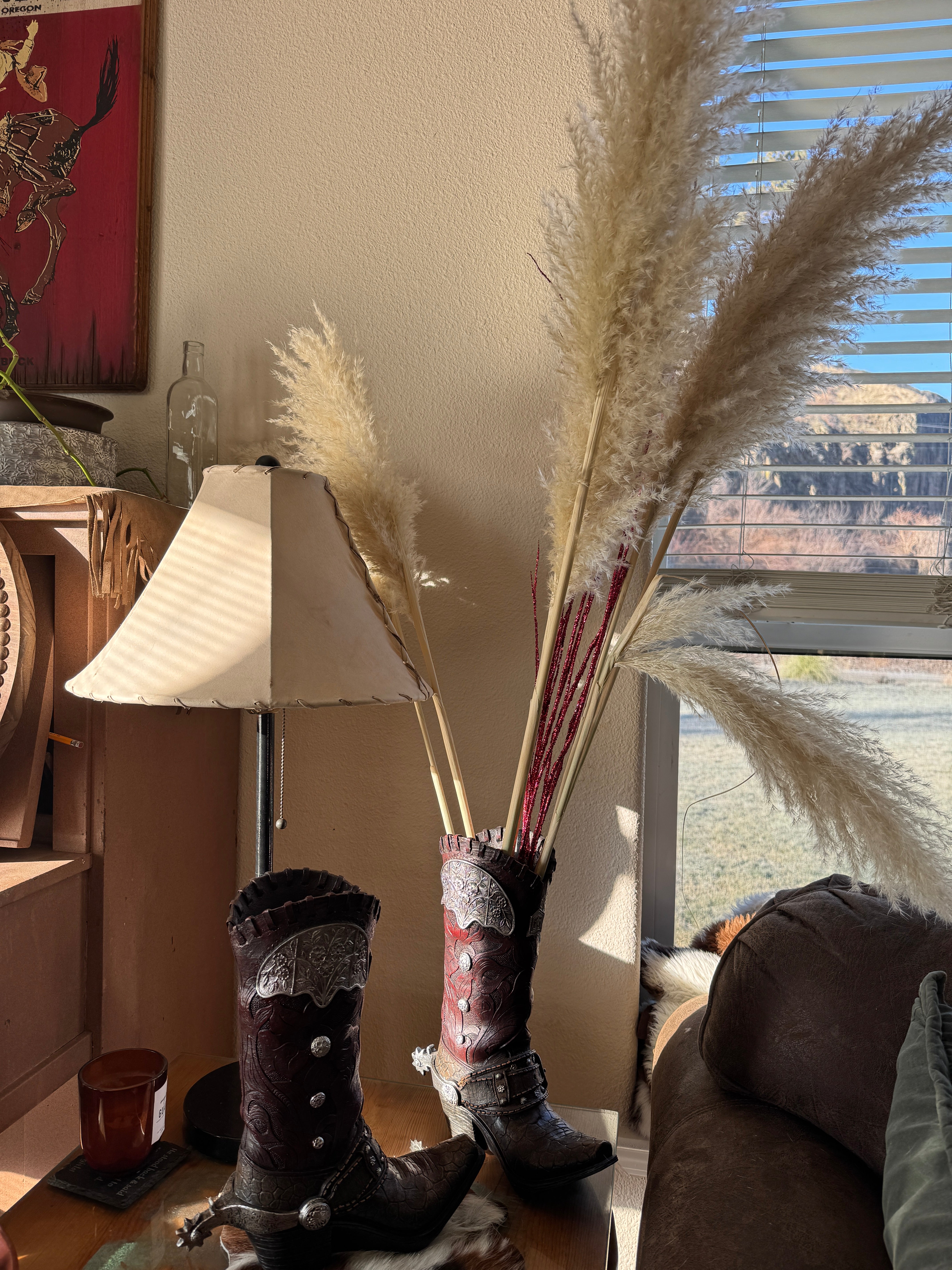 Decorative elements including pampas grass in cowboy boot vase, rawhide lamp shade, and a decorative item on a surface with a window in the background.
