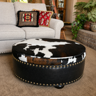 Luxury western living room featuring a tri-color cowhide cocktail ottoman with black leather trim and rustic ranch furnishings.