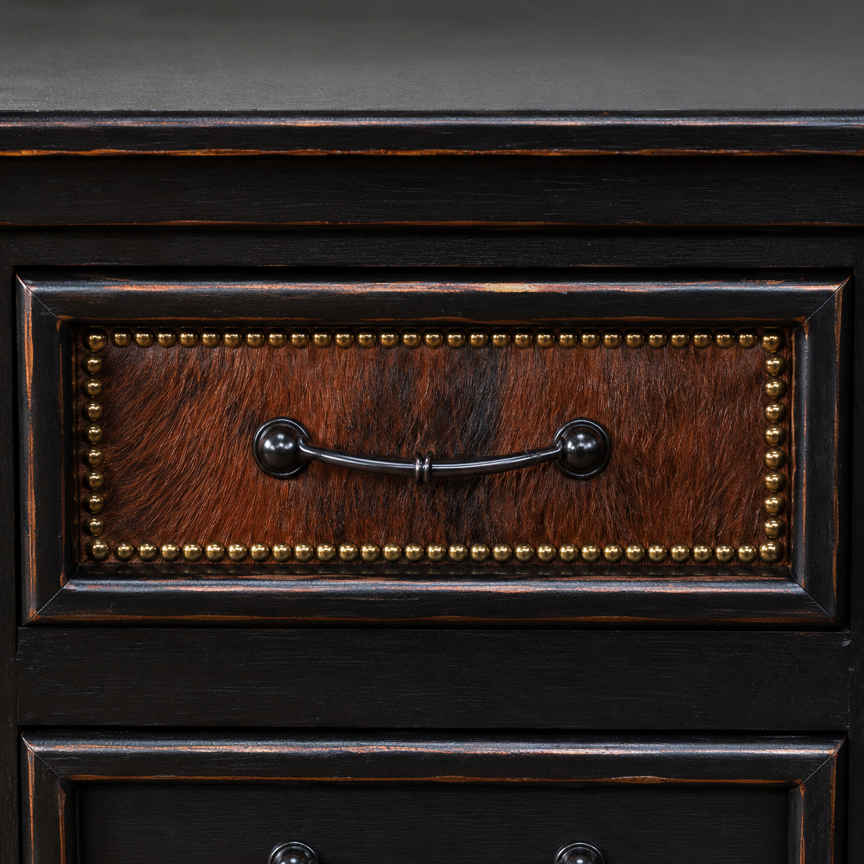 Detail image of brindle cowhide, nailhead trim, and black iron drawer pull detail on nightstand 