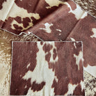 A close-up of a brown and cream cowhide-patterned table runner and placemat on a peppered brown-and-white cowhide rug 