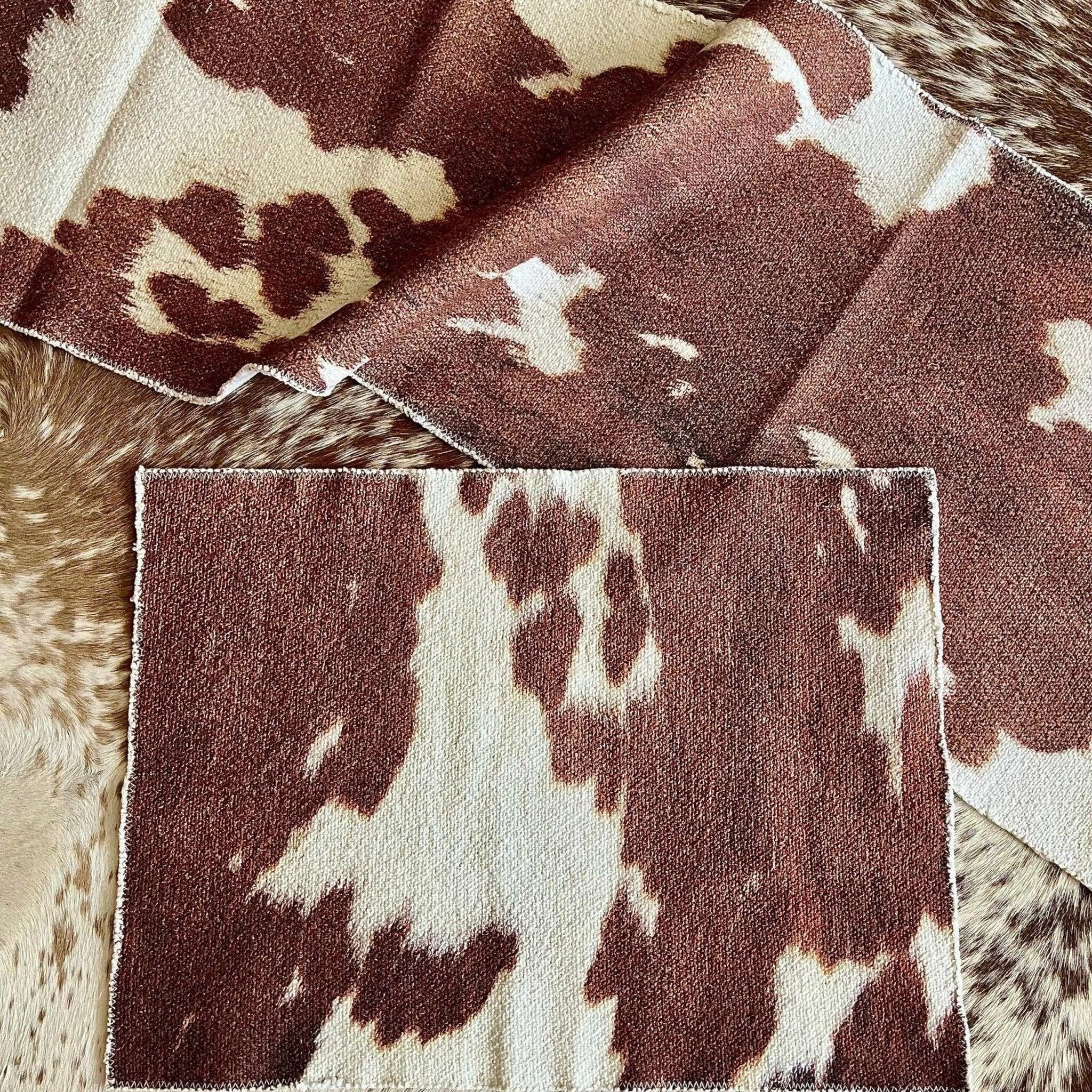 A close-up of a brown and cream cowhide-patterned table runner and placemat on a peppered brown-and-white cowhide rug 