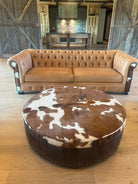 round cowhide ottoman with brown and white hide top and leather sides with Chesterfield sofa western furniture