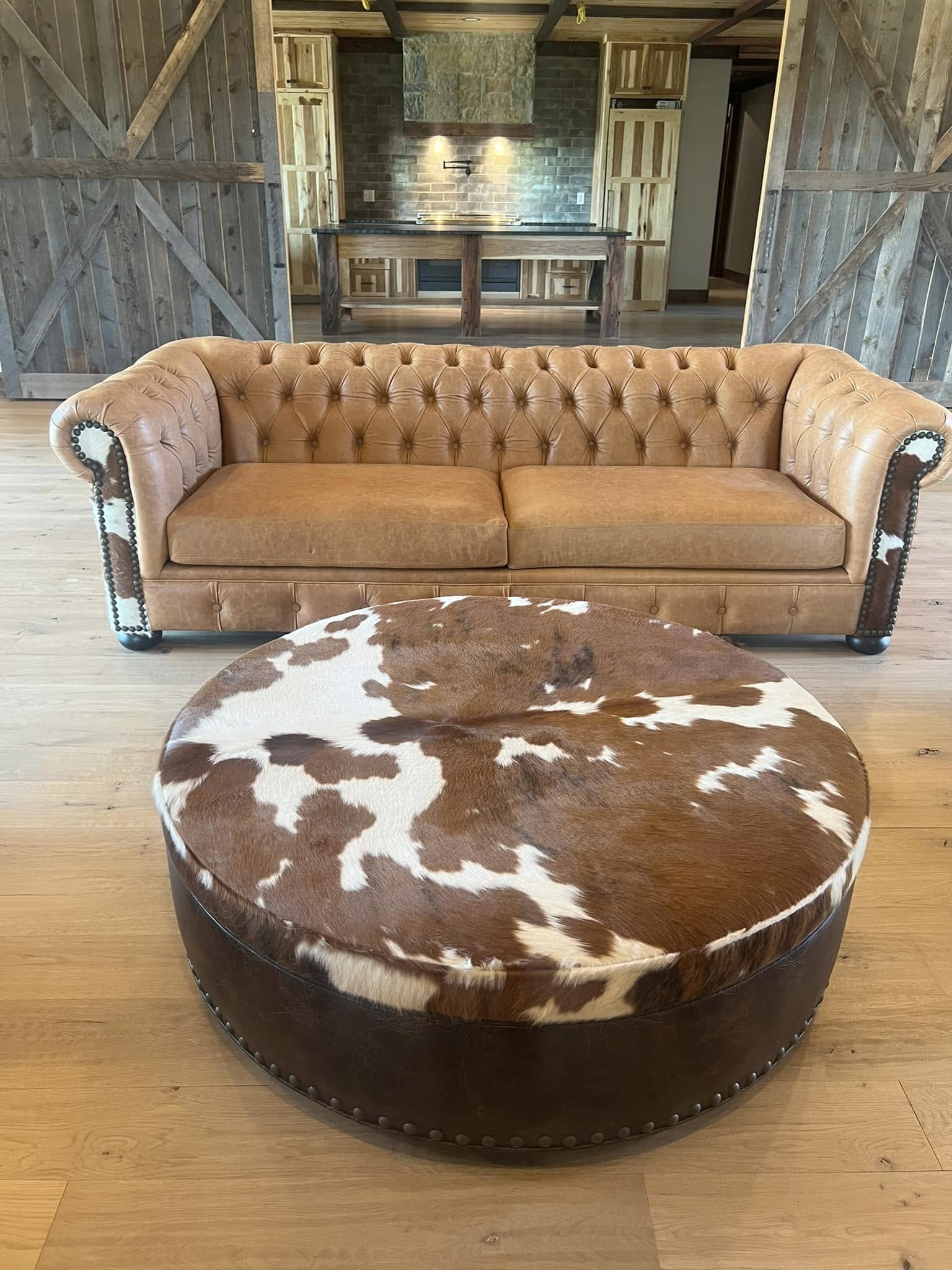 round cowhide ottoman with brown and white hide top and leather sides with Chesterfield sofa western furniture
