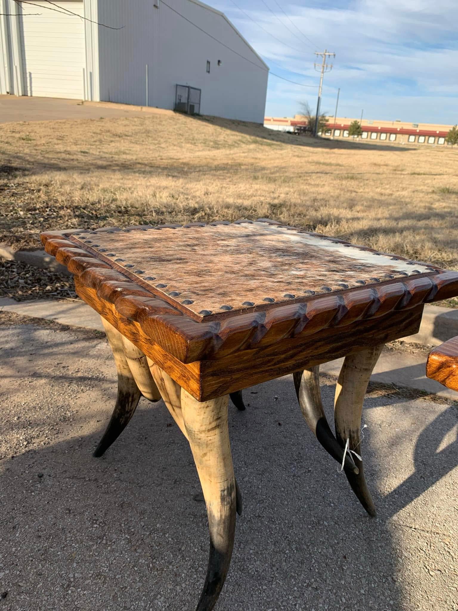Wood-top western side table with carved rope detail, cowhide upholstered top with nail trim standing on steer horn legs